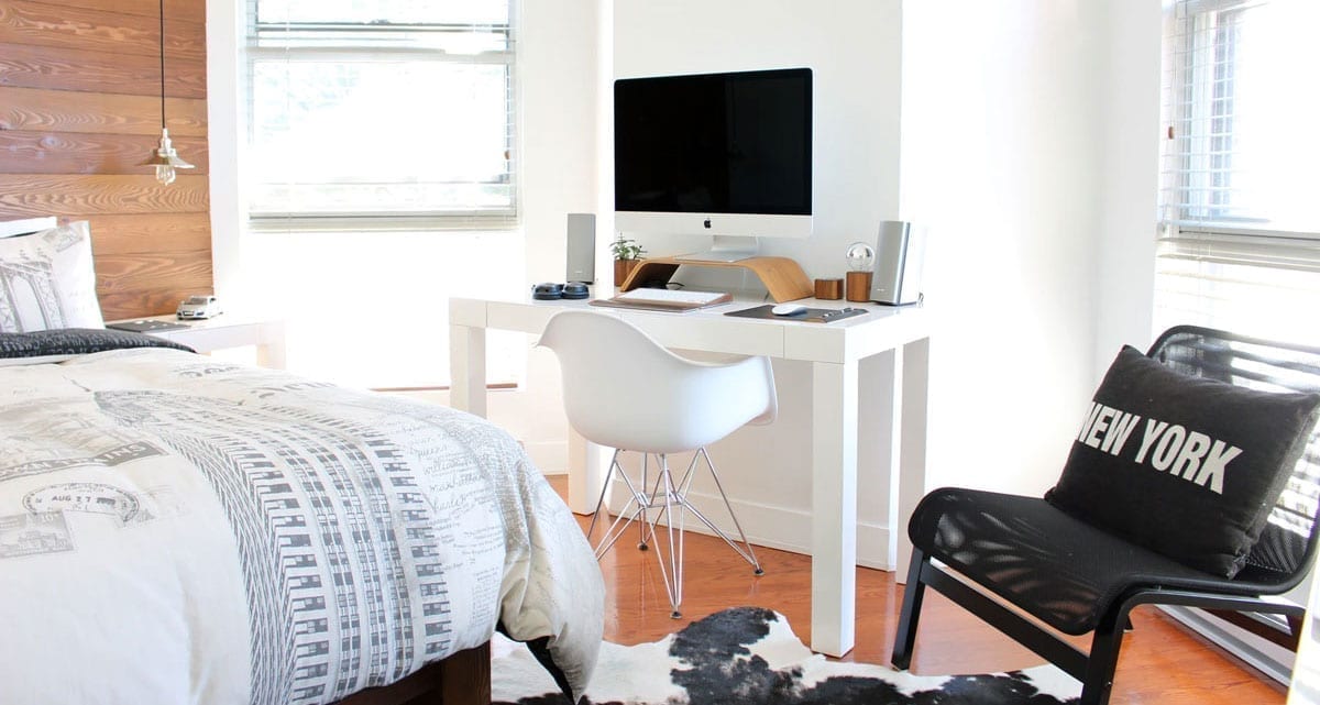 White walled naturally lit homeschool classroom workstation in a person's bedroom complete with comfy chair and cow skin rug.