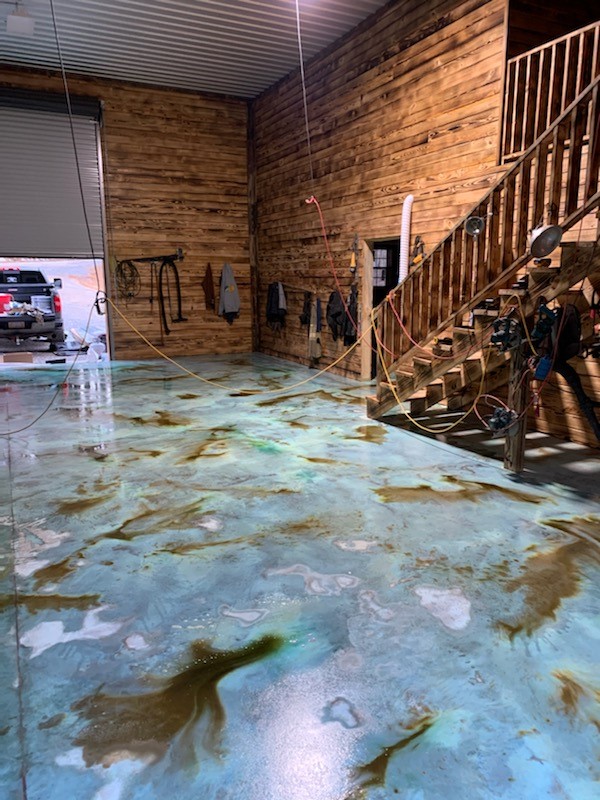 A wet azure blue stained concrete garage floor, fresh from sealer application, with hints of shifting sand accents creating an oceanic ambiance