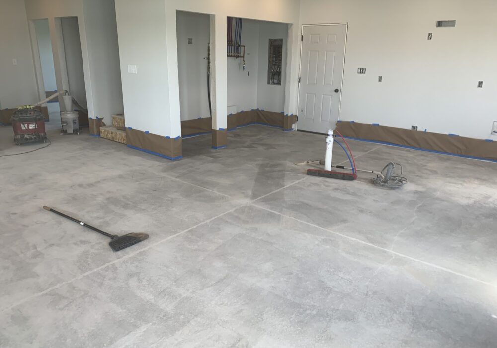 Freshly ground concrete floor of a cabin with a broom laid across, indicating recent cleaning