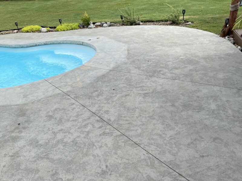 A worn-out, discolored stamped concrete pool deck before restoration