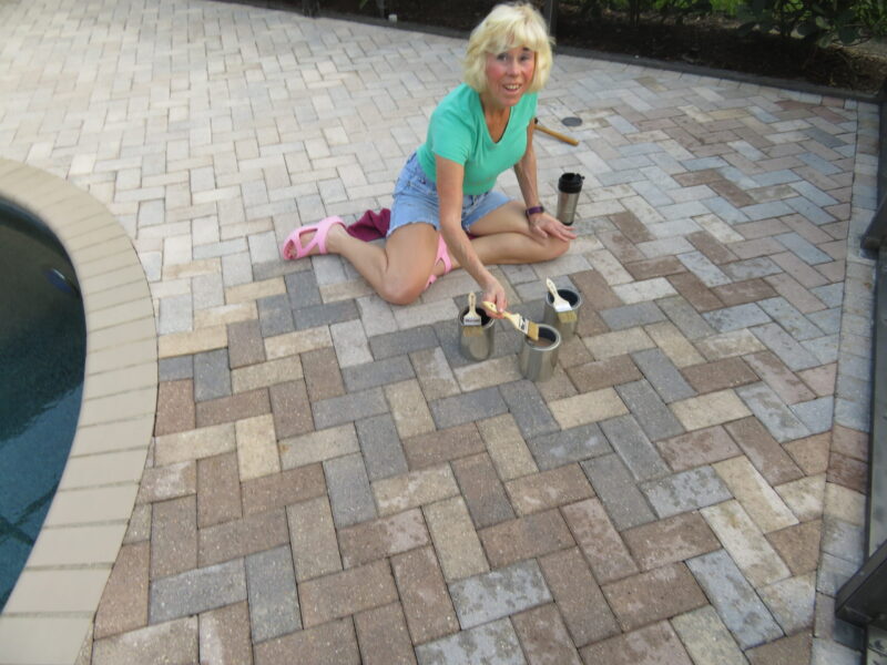 Woman meticulously staining each paver around the pool using paint brushes