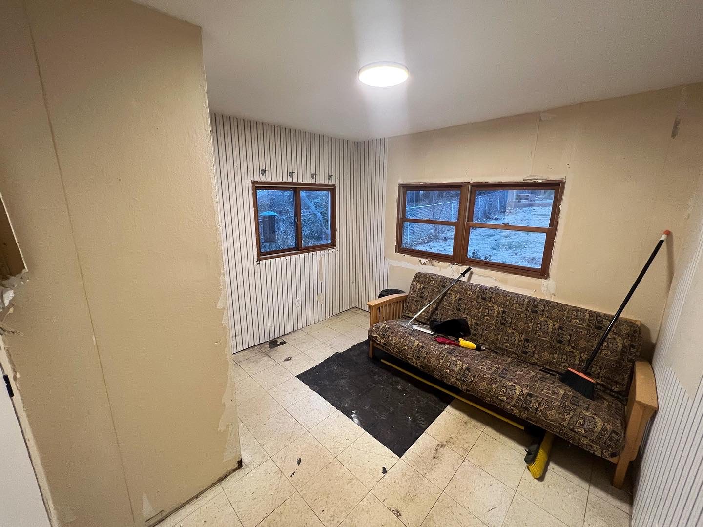 DIYer using a floor scraper to remove old linoleum tile and mastic from a concrete floor