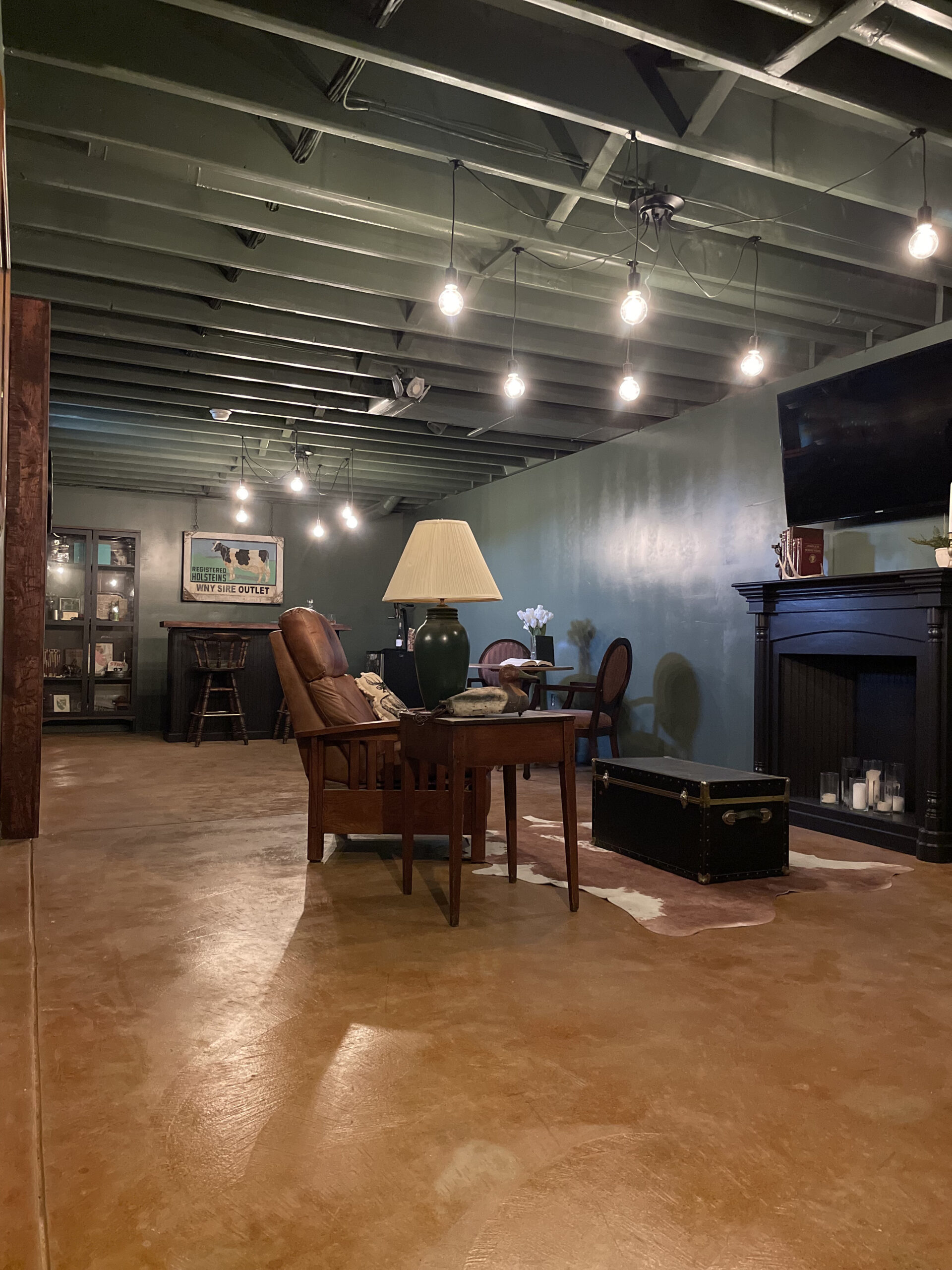Image featuring a cozy set-up with two reclining leather chairs, a cowhide rug, and string lights above