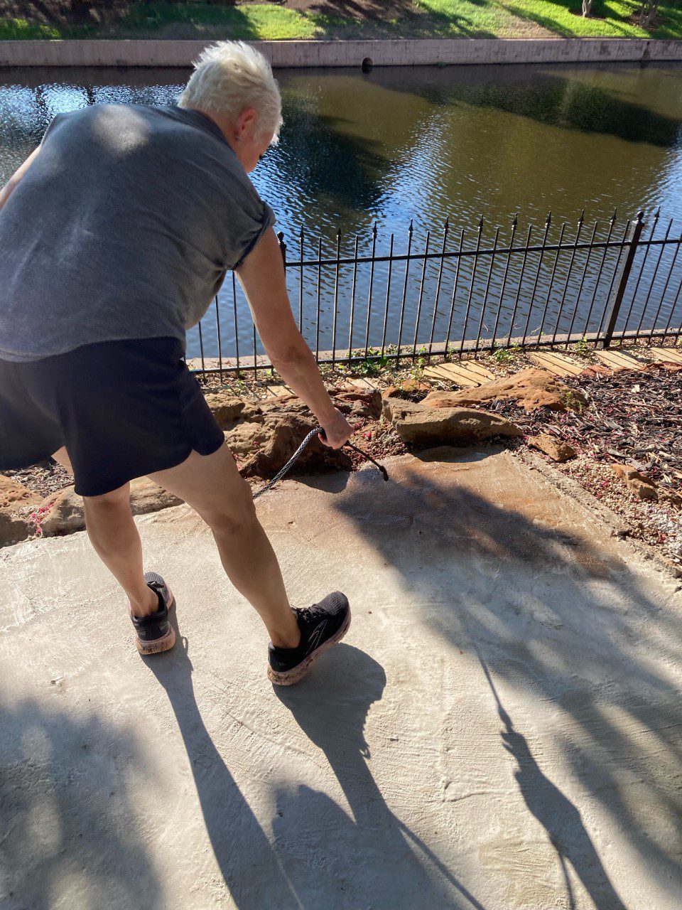 A woman skillfully applying Antiquing Cafe Royale stain to her cured DIY poured concrete patio, enhancing its visual appeal and character.
