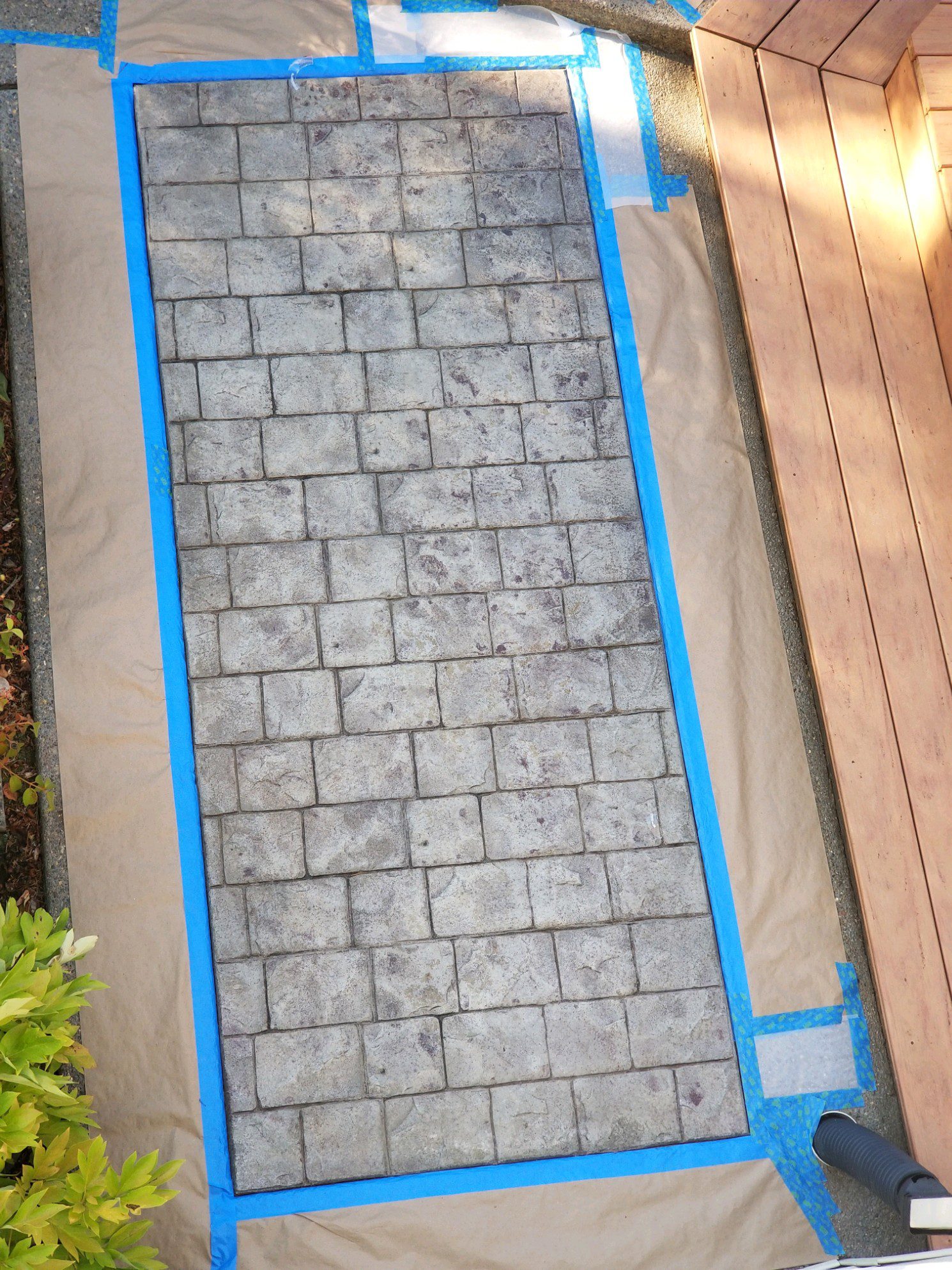 Prepped patio area with faded stamped concrete, covered edges with masking tape and paper to protect from Cinnabar stain application