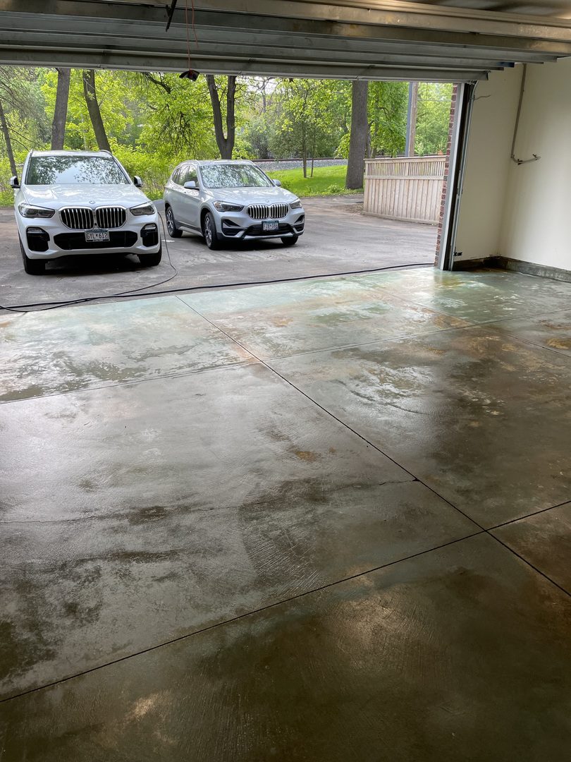 A view from the inside of a finished garage, light-green stained floor gleaming, with cars parked outside waiting for the sealer to cure