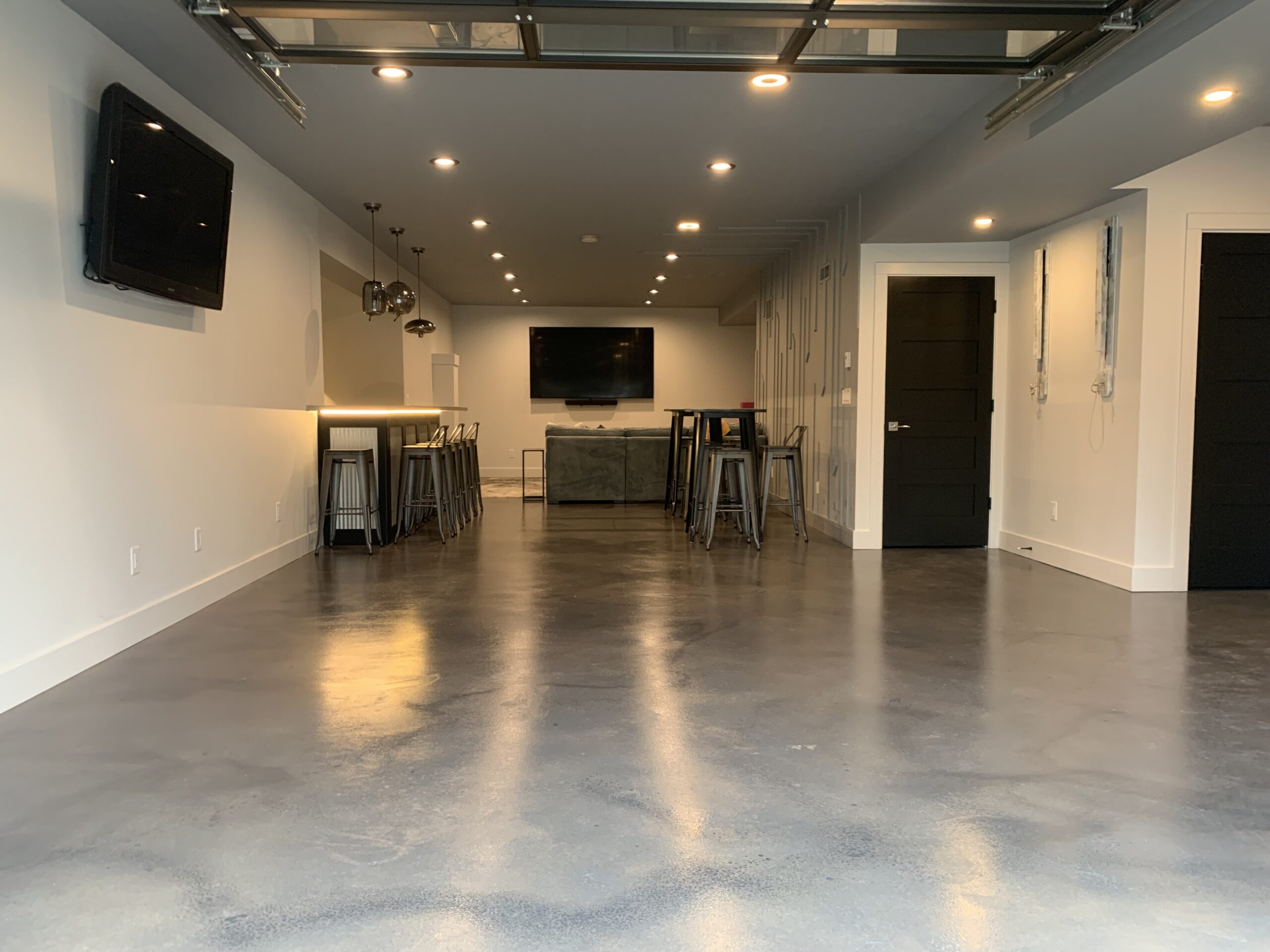 A basement with protective coverings on the lower walls and bar, showing the floor after the application of the first coat of AcquaTint stain.