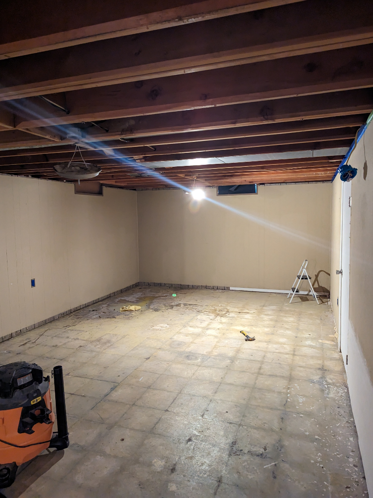 A basement floor covered in mastic, showing the ghosting of removed poly tiles before concrete staining
