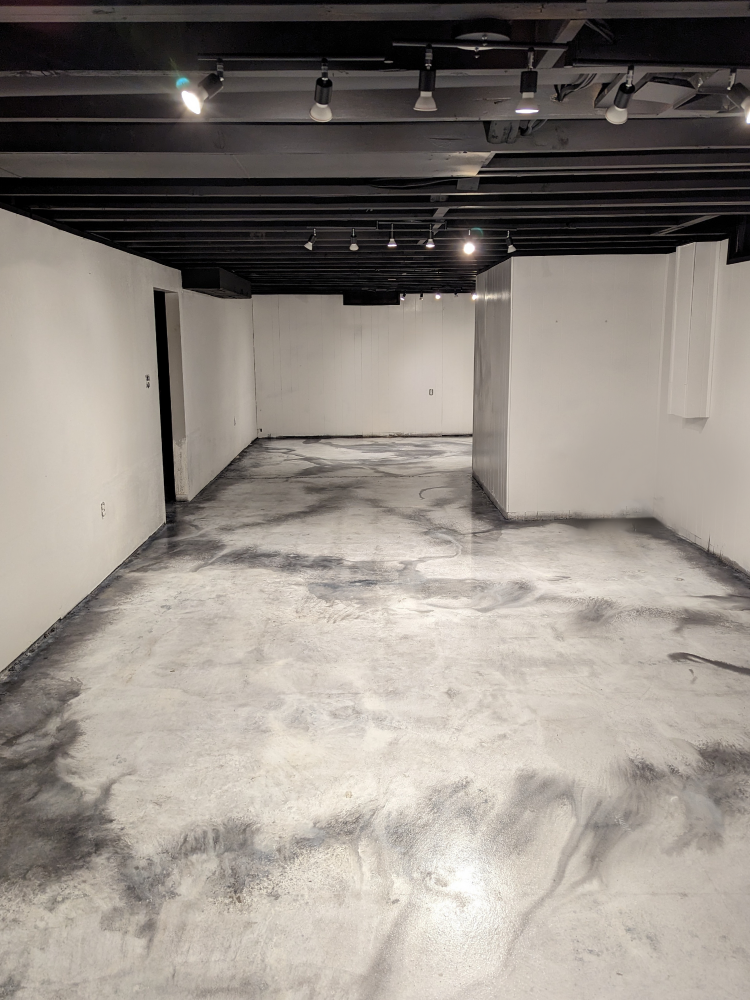 A basement floor stained with ColorWave in White and Steel after mastic removal, creating a sleek marbled effect
