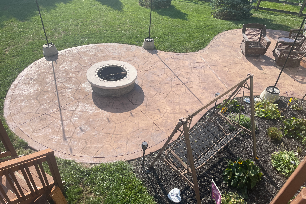 Faded stamped concrete patio with fire pit before restaining, showing dull color and surface wear.