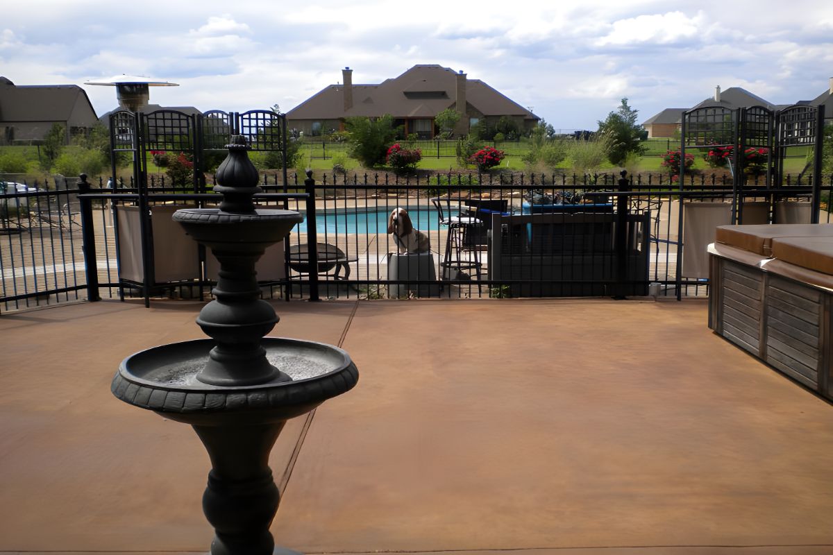 Broom-finished concrete patio stained with Café Royale Antiquing™ Stain, featuring a rich, warm brown tone near a pool and fountain.