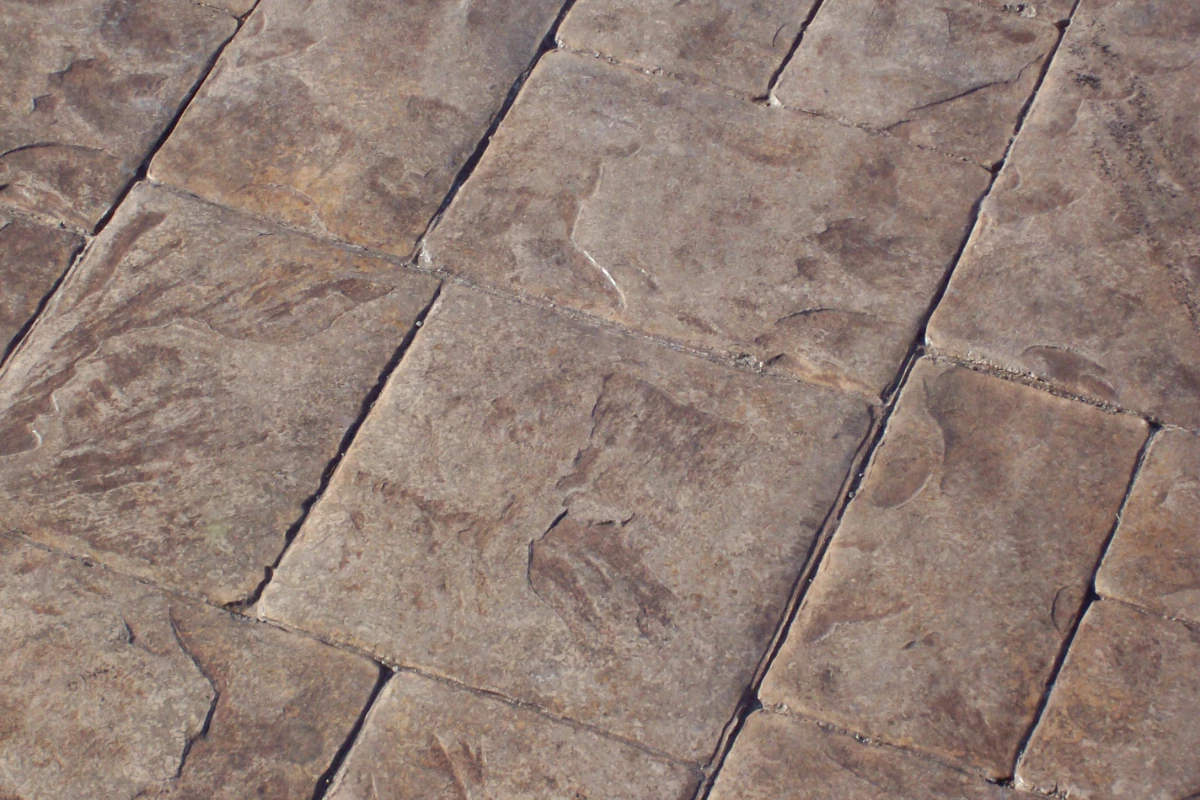 Close-up of stamped concrete patio colored with Auburn Antiquing Stain, showing natural brown tone and detailed texture pattern.