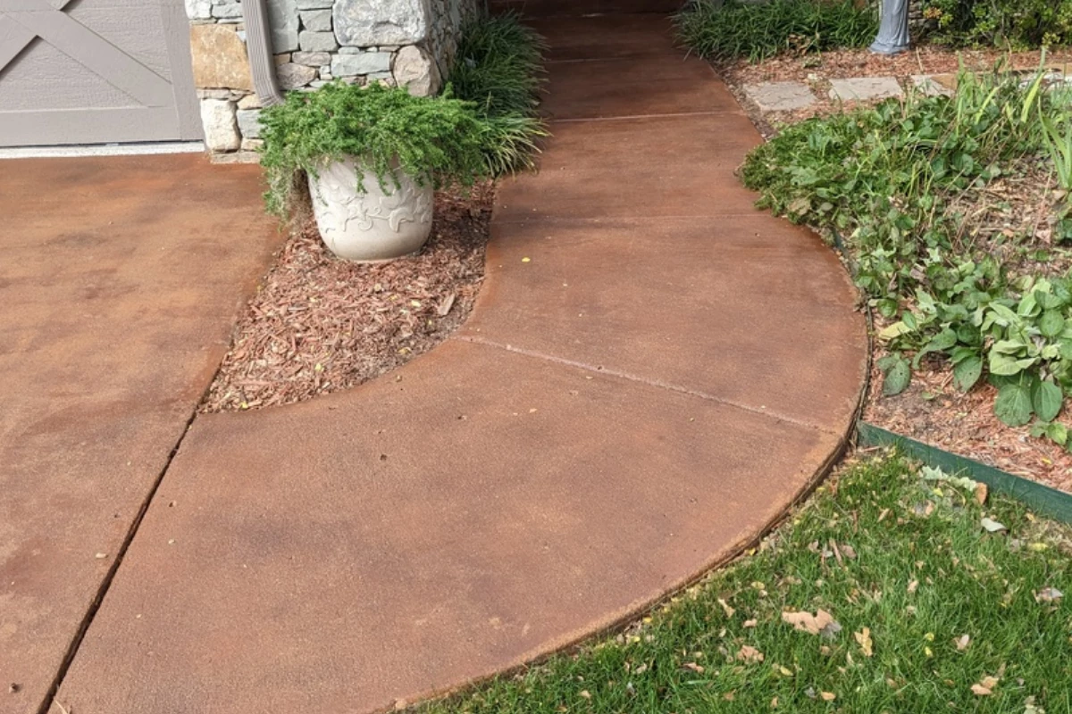 Curved front walkway finished with Aztec Brown stain and sealed in gloss, complementing stone exterior and landscaping.