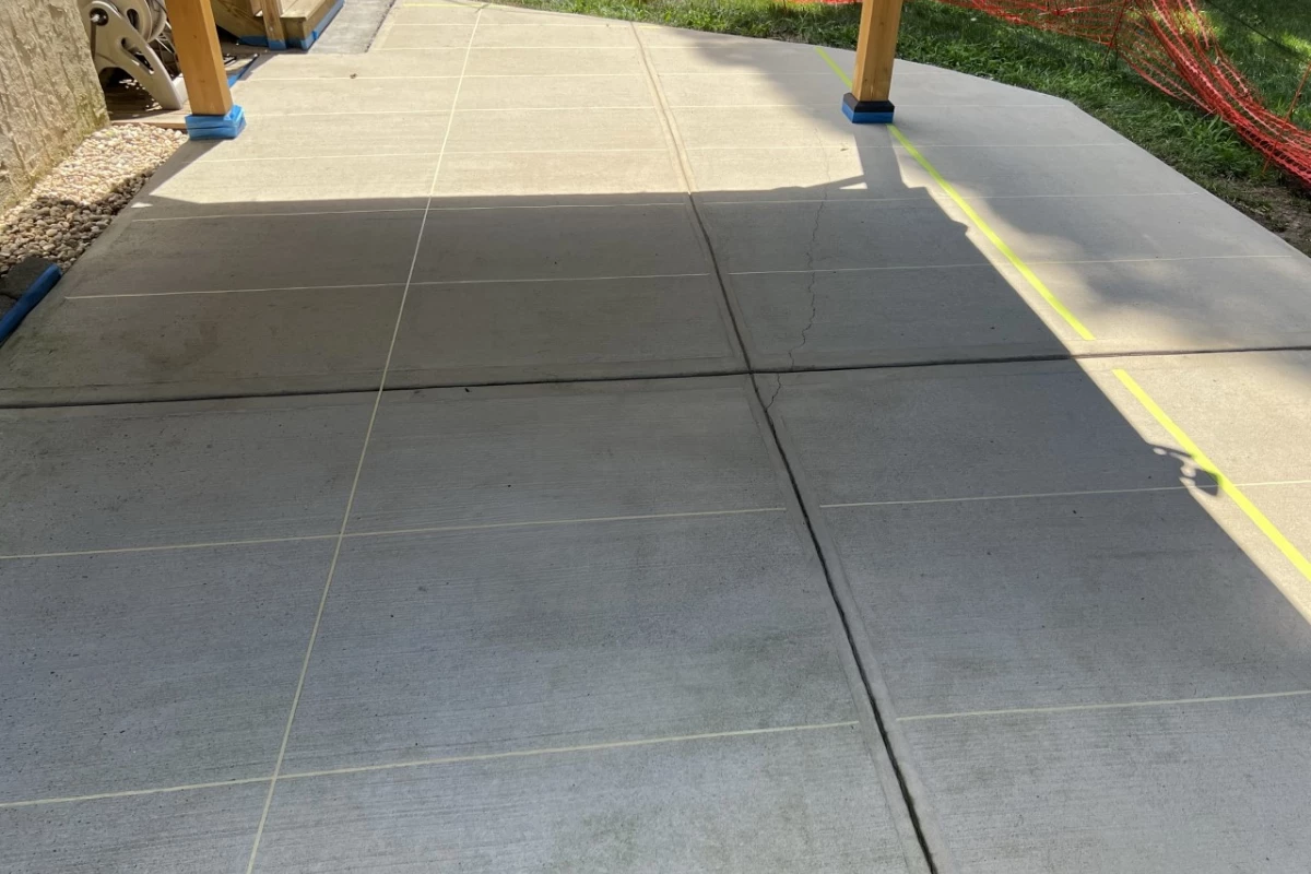 Covered scored concrete patio surface with tape creating a large tile design pattern, ready for staining.