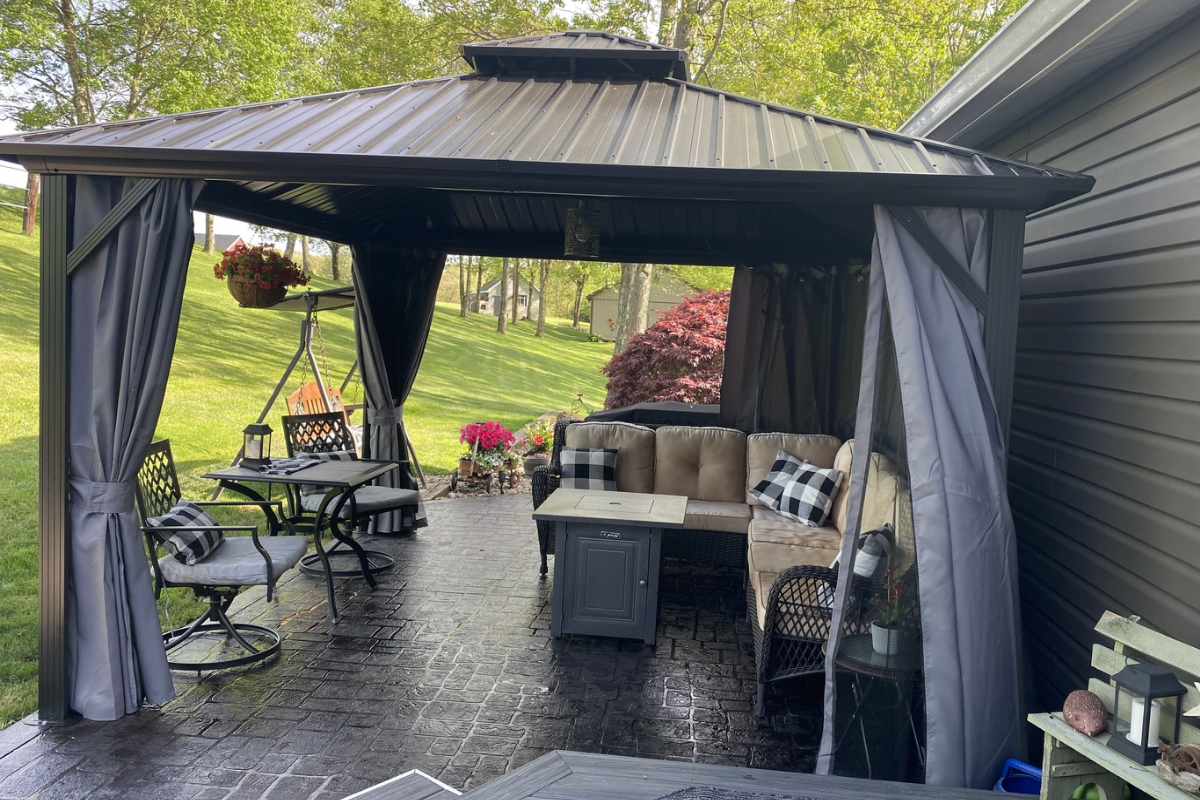 A cozy outdoor patio under a gazebo with comfortable seating and a stamped concrete floor stained in a sleek black finish