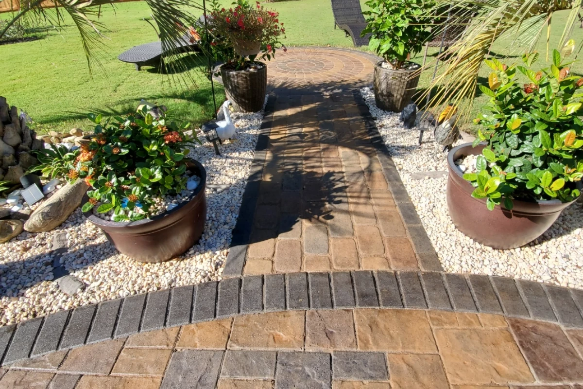 Wide view of a finished backyard patio with vibrant multi-tone pavers, tropical landscaping, and a fountain centerpiece.