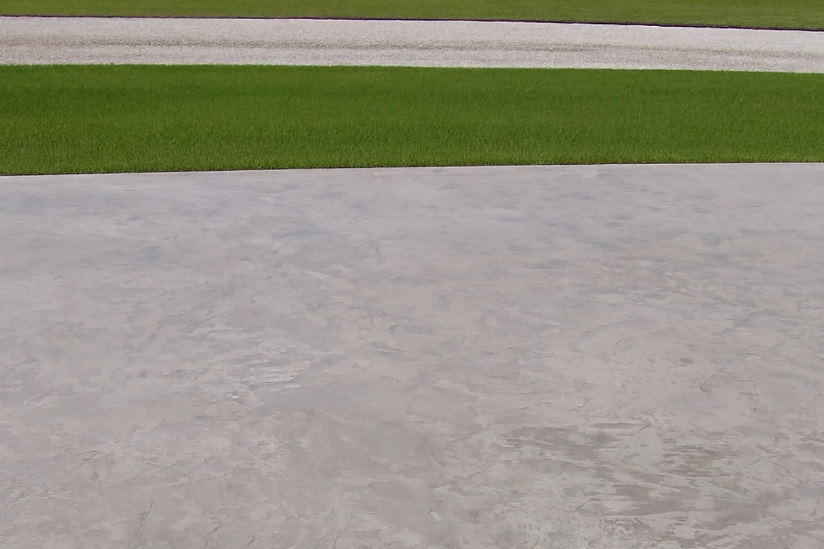 Faded stamped concrete driveway before color restoration with Auburn Antiquing Stain, showing light gray worn surface.