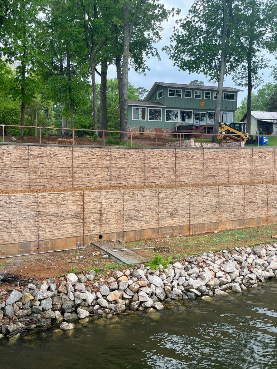 Large lakeside concrete retaining wall stained with Café Royale EasyTint™, featuring warm tan and brown tones that mimic natural stone under a tree-lined landscape.