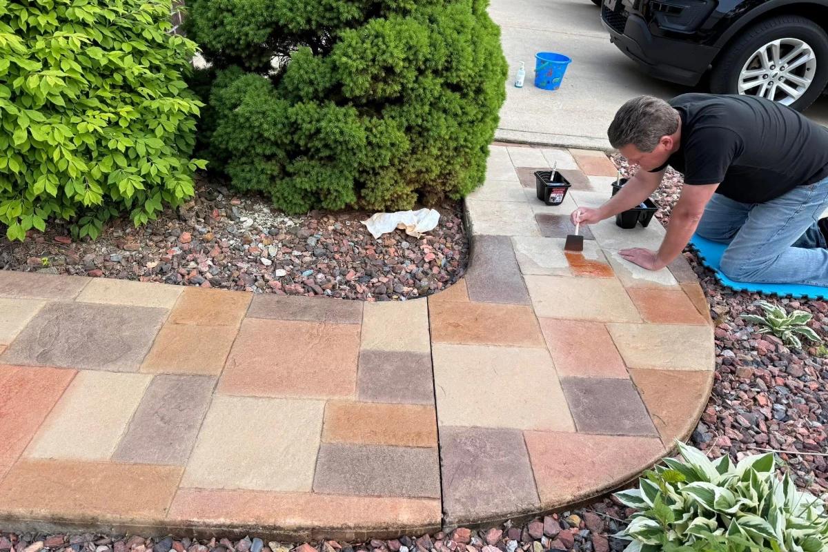 Homeowner applying Auburn Antiquing Stain with a brush to refresh faded stamped concrete walkway.