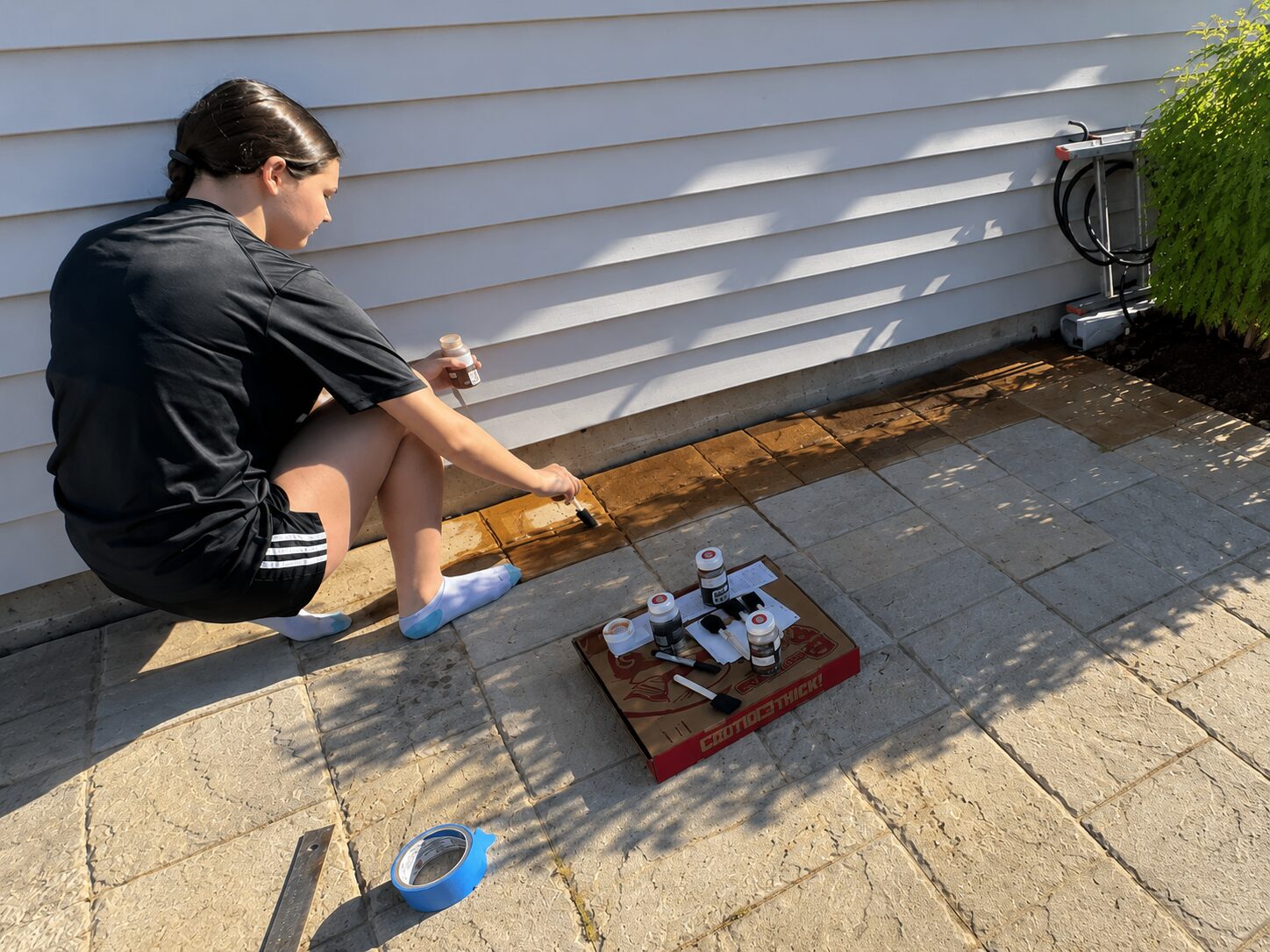 Young customer applying Antiquing stain to stamped concrete patio with a foam brush for a multicolor paver-style finish.
