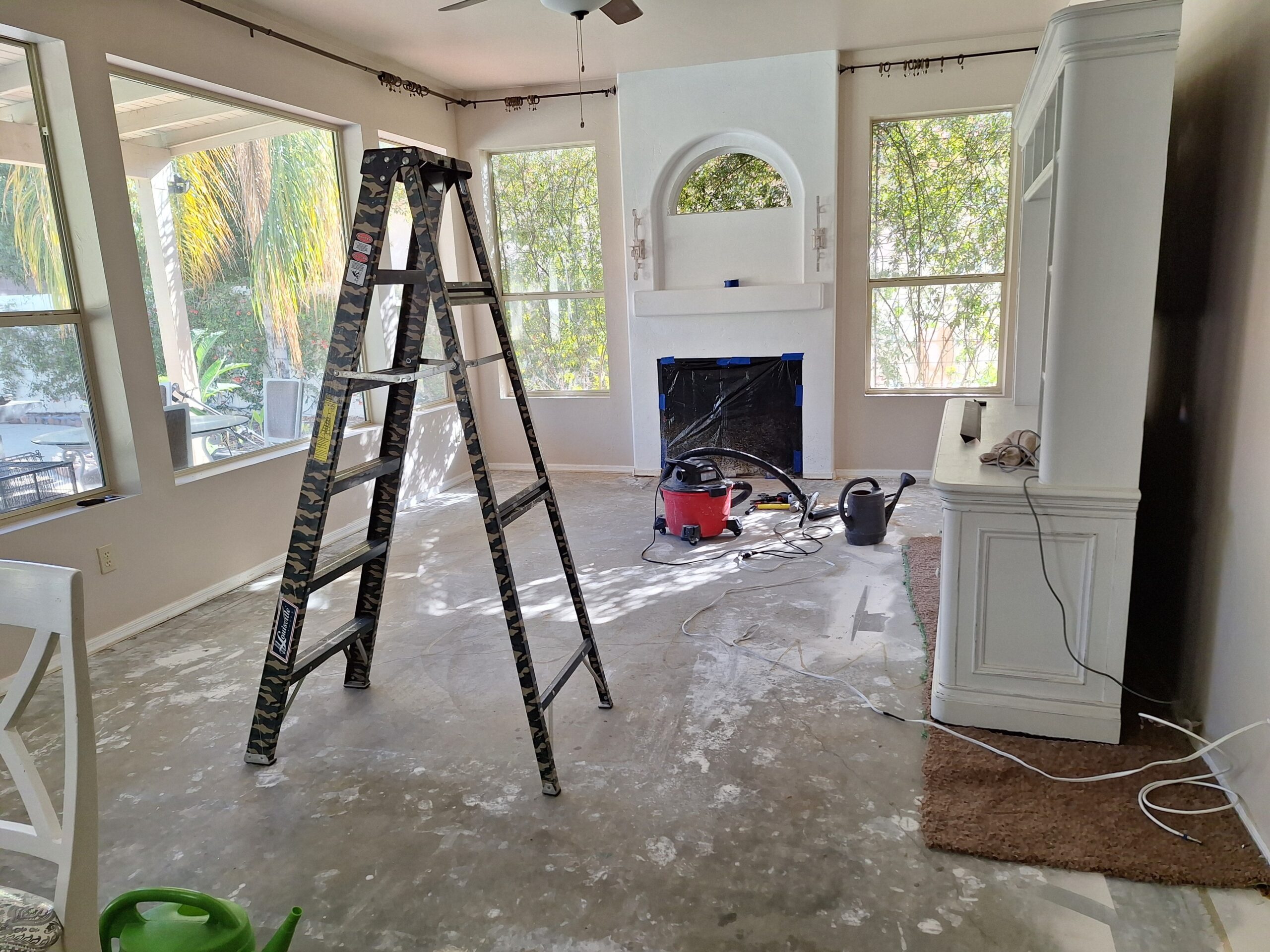 Living room with carpet removed, exposed concrete floor, prep tools, ladder, and fireplace before applying ColorWave Stone concrete stain.