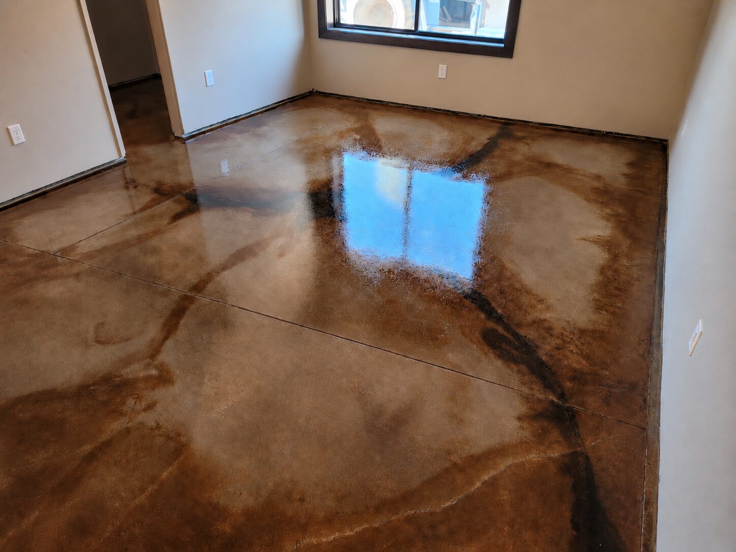 Residential room with EverStain Black, Desert Amber, and Malayan Buff acid-stained concrete floor, showing a glossy brown marbled finish with dark veining.