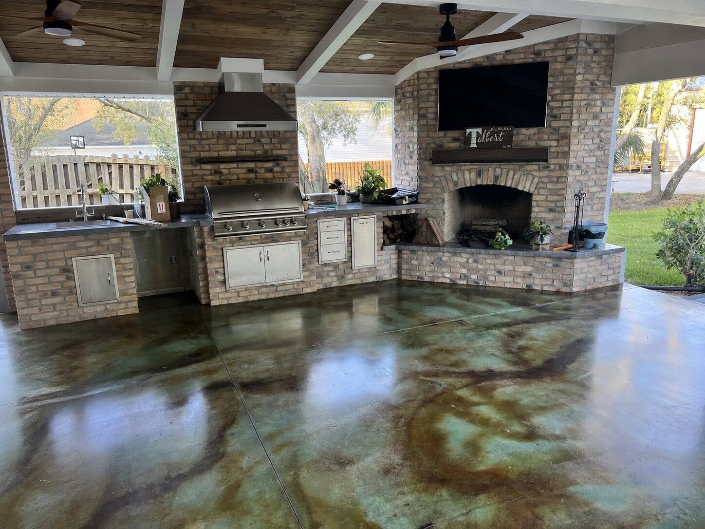 Covered outdoor kitchen with EverStain Malayan Buff and Seagrass acid-stained concrete floor, showing a glossy blue-green and brown marbled finish.