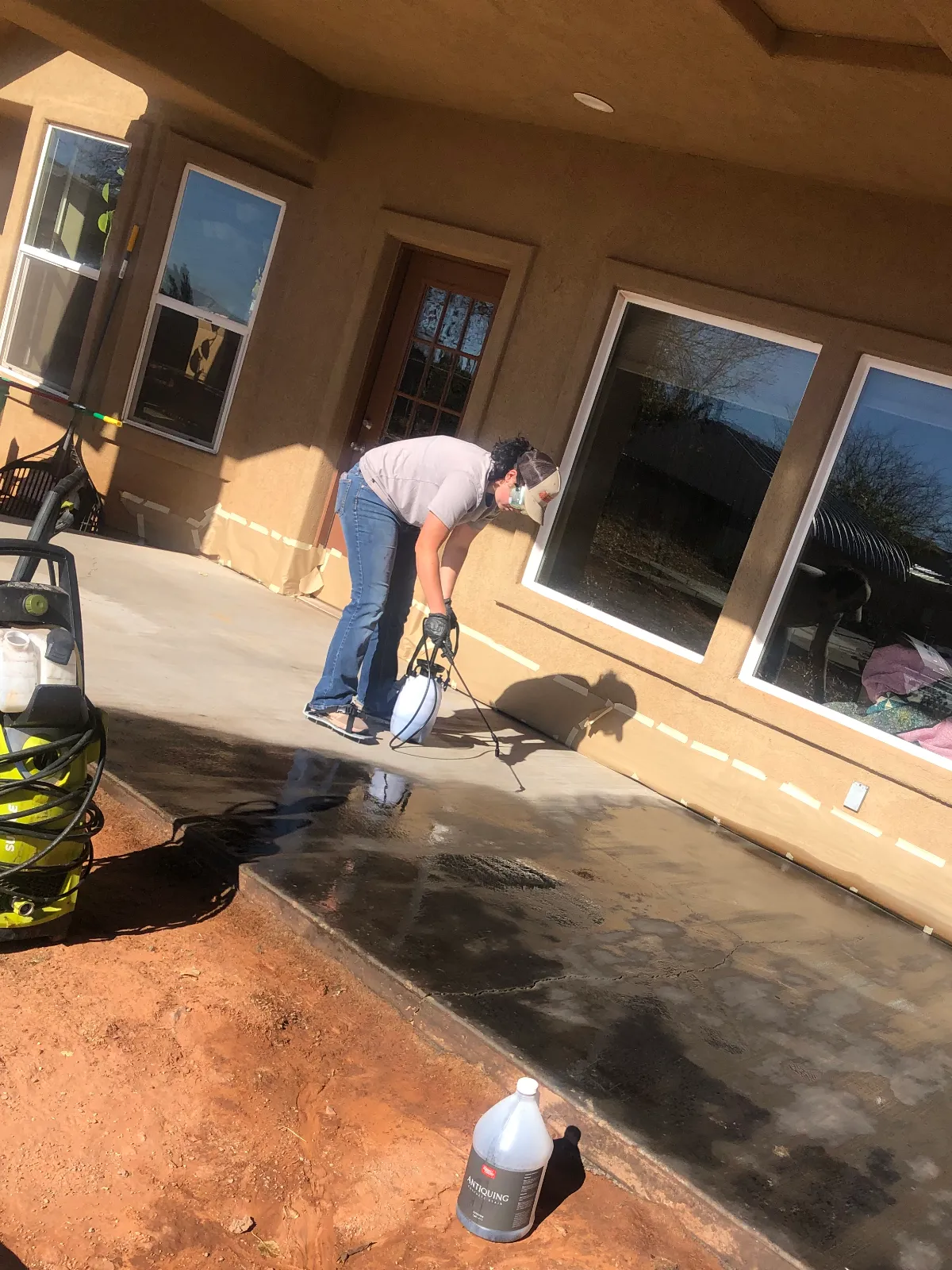 DIY homeowner wearing spiked shoes and spraying Black Antiquing Stain onto a broom-finish concrete patio.