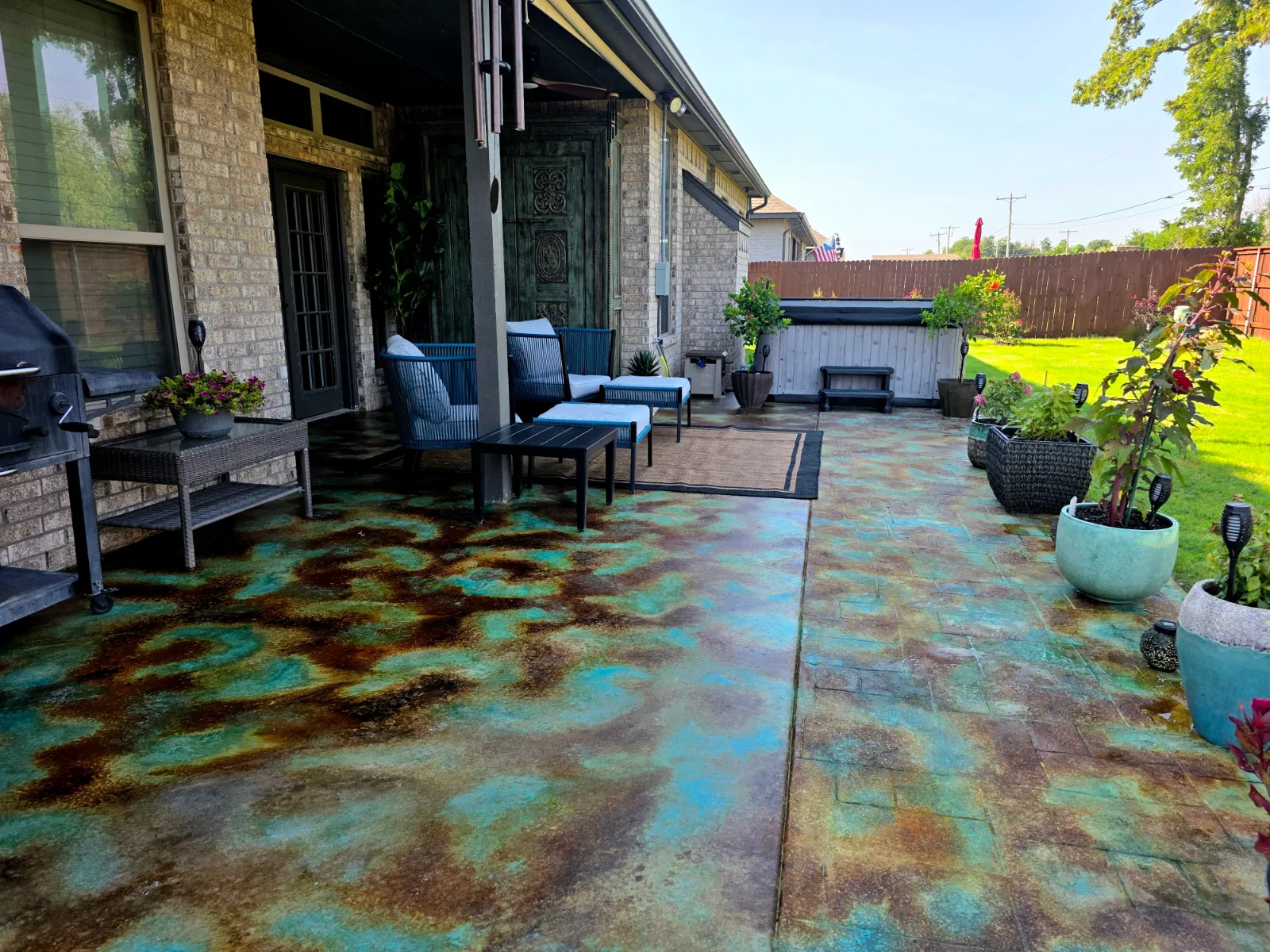 Smooth and stamped concrete patio acid stained in a blue and copper patina with Azure Blue, Desert Amber, Cola, and Coffee Brown EverStain, furnished with a seating area and hot tub