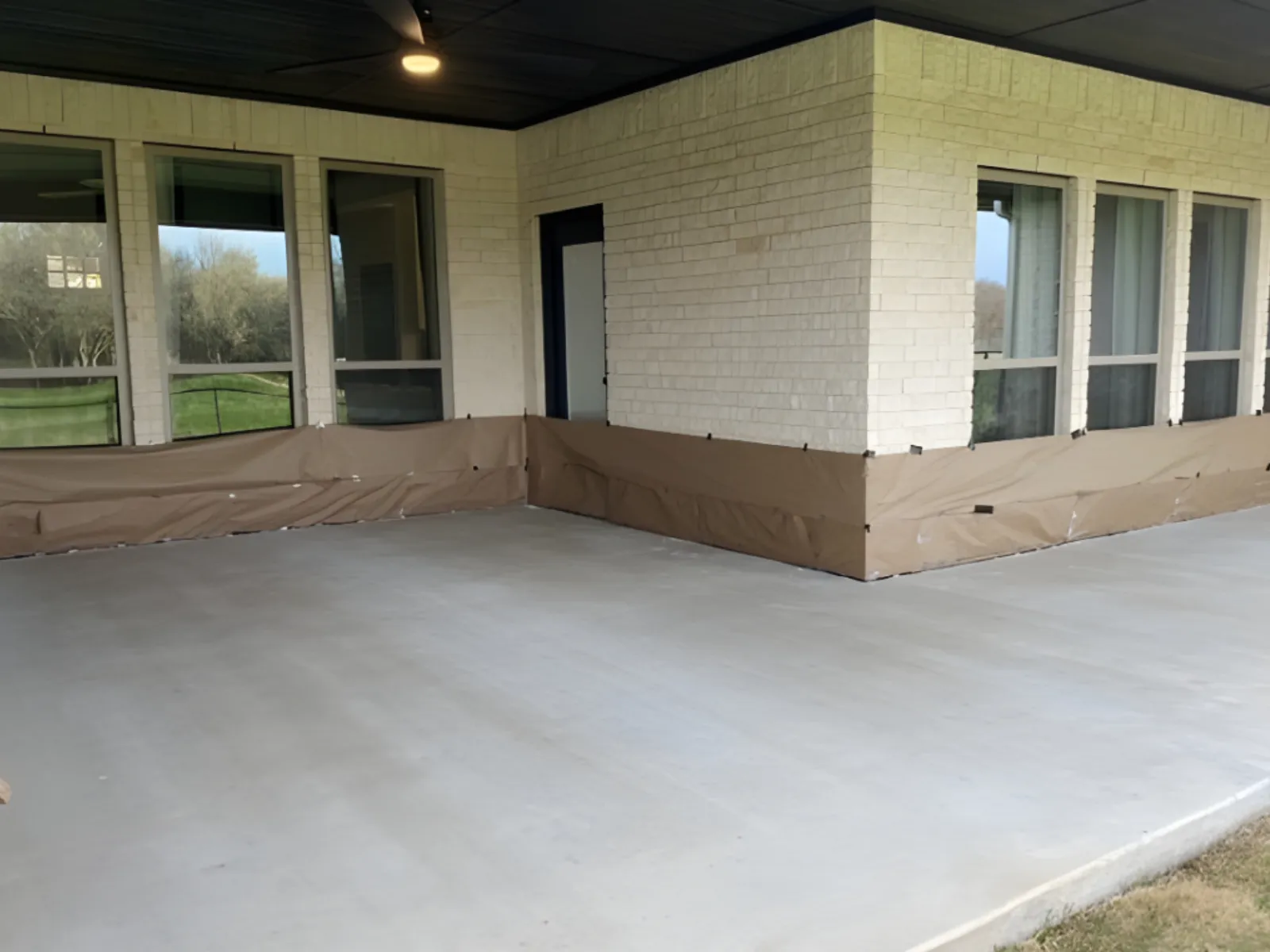 Plain 433-square-foot covered smooth concrete patio masked and prepared for Black Antiquing Stain.