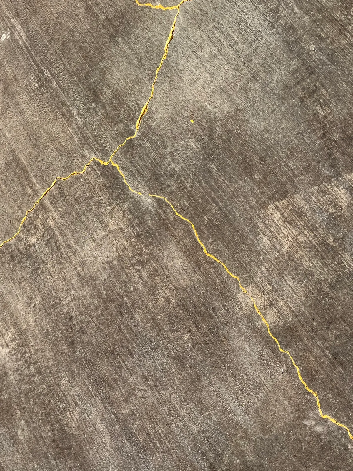 Close-up of a black-stained concrete patio featuring natural cracks highlighted with gold acrylic paint.