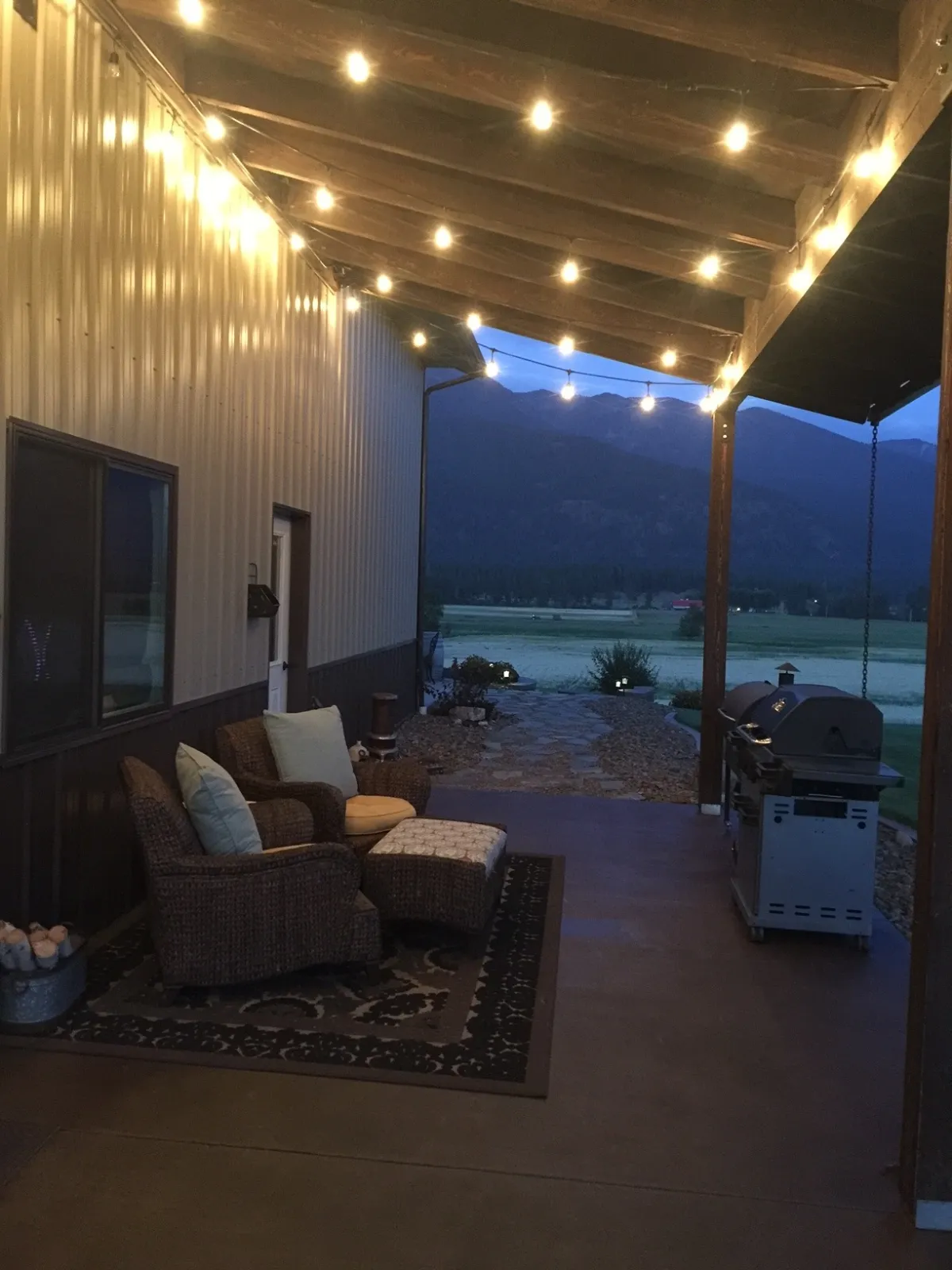 Furnished pole barn concrete porch stained with Driftwood Antiquing Stain and illuminated by string lights at dusk.