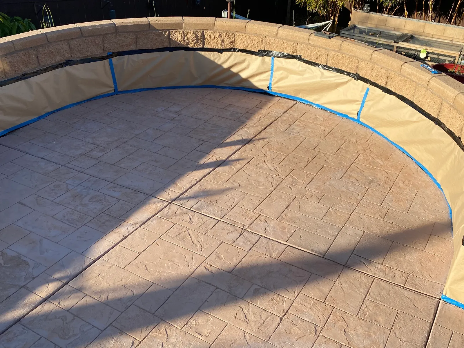 Previously integrally colored stamped concrete patio faded to pale pink and masked before applying Crimson Antiquing Stain.
