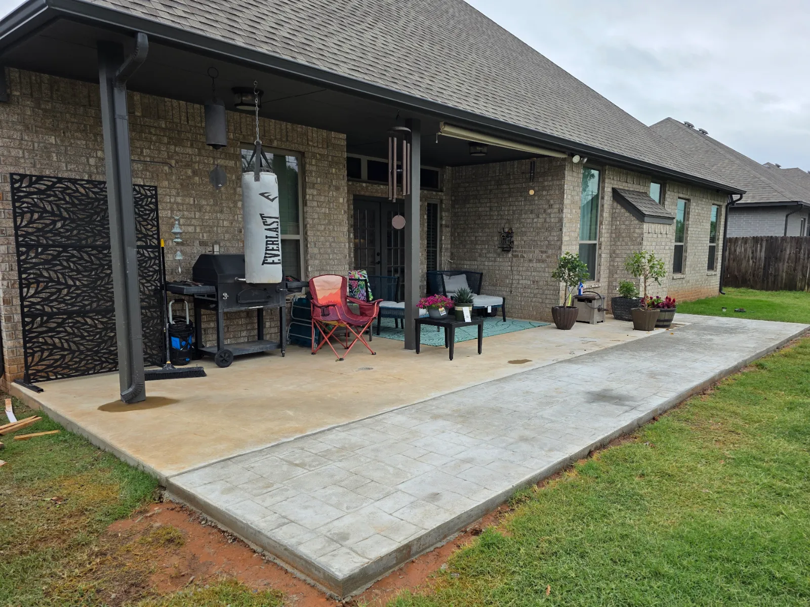 Plain tan concrete patio before acid staining, showing a smooth original slab and a newly added stamped concrete extension on a covered brick home in Oklahoma