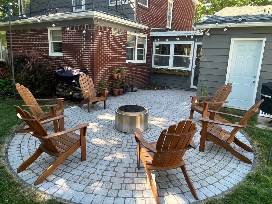 Whitewashed circular paver patio styled with a fire pit and wooden Adirondack chairs, finished in PaveWave White